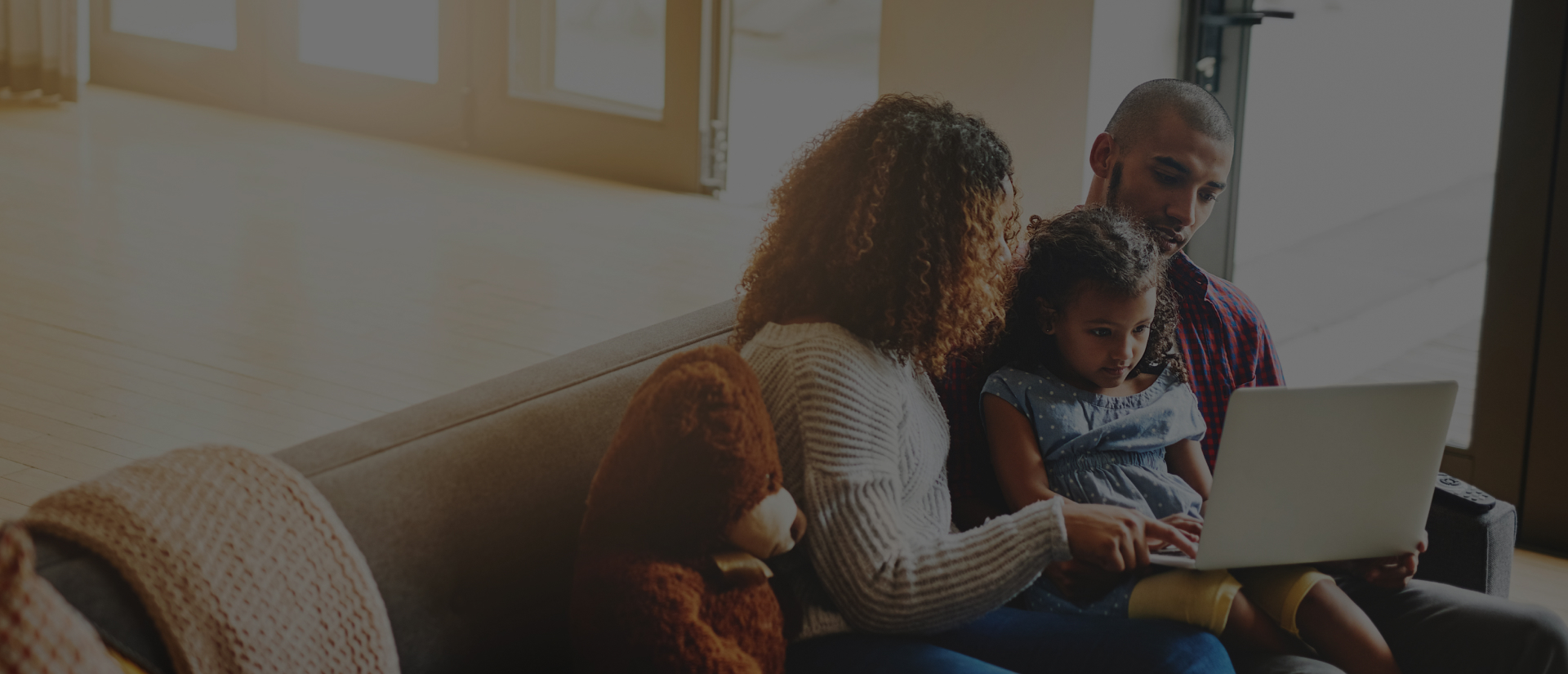 Family sitting on couch using a laptop together in a cozy living room